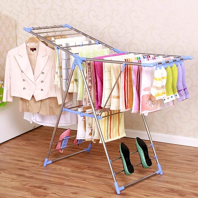 Indoor clothes drying rack filled with pastel towels and a light pink blazer, standing on a wooden floor with a pair of green heels nearby.
