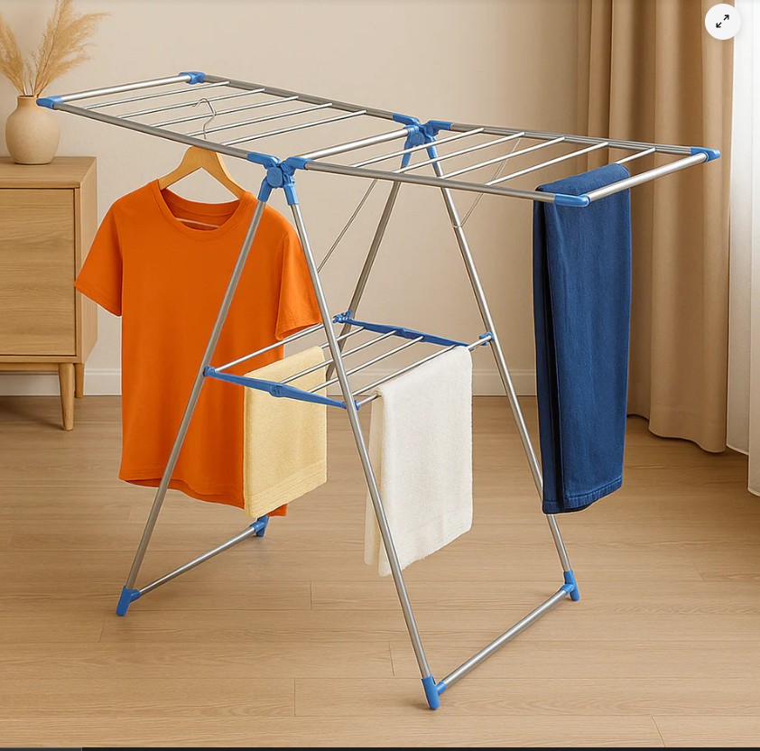 Foldable metal drying rack in a sunny room with clothes hanging to dry (orange T-shirt, towels, and blue jeans).