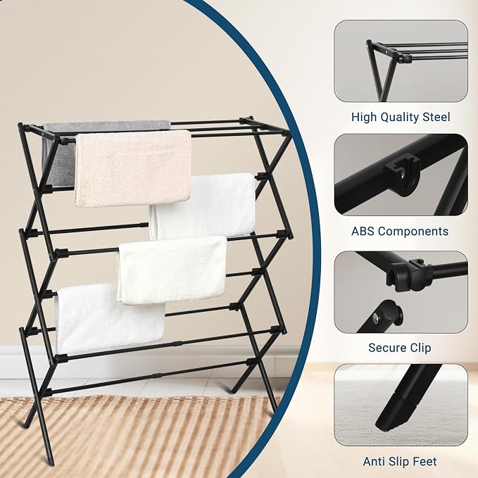 Foldable black metal drying rack with towels hanging on it, placed beside a rug in a room.